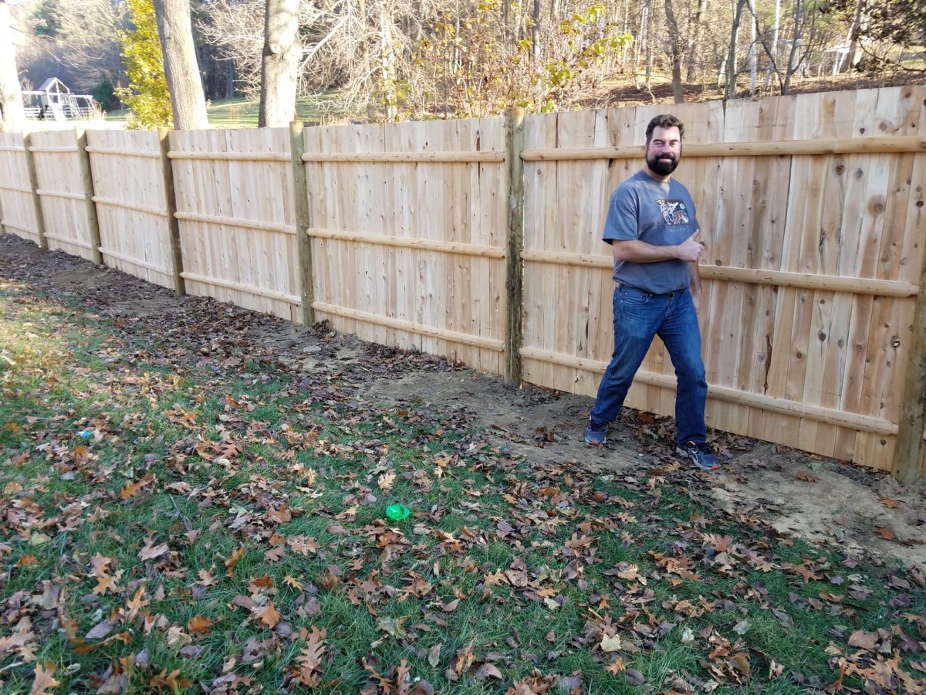 Newly installed natural cedar stockade privacy fence in a wooded back yard